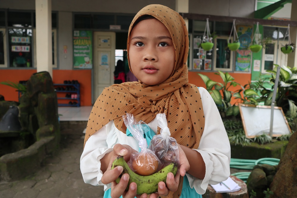 PAKET HEMAT: Salah satu siswa SD di Kecamatan Pesantren menunjukkan menu kurma, pisang, dan satu butir telur rebus yang diterimanya di bulan Ramadan.