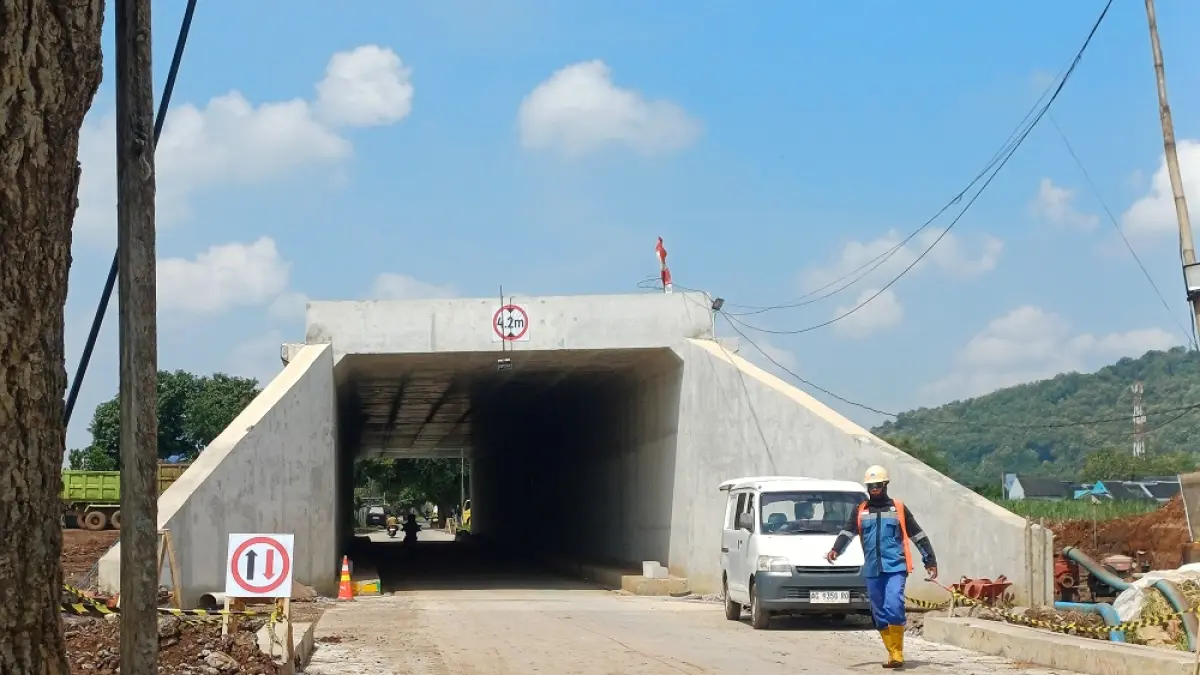 Seorang pekerja proyek melintas di depan underpass Tol Kediri-Tulungagung akses Bandara Dhoho di Kelurahan Bujel. (Foto: Ayu Isma)