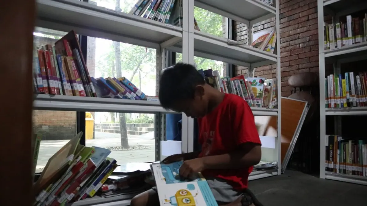LESEHAN: Albert, 8, asyik membaca buku bergambar di Pojok Baca Taman Sekartaji, Kota Kediri saat anak-anak seusianya berlarian dan bermain di taman barat sungai itu.