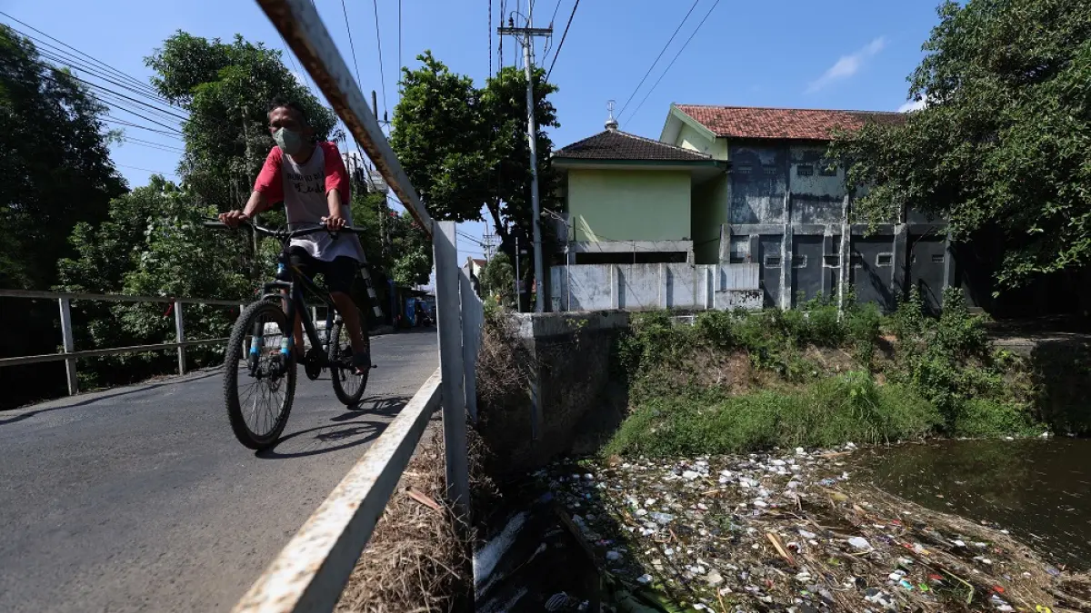 DIPENUHI SAMPAH: Pesepeda melintas di jembatan Kelurahan Bujel Gang 4, Kecamatan Mojoroto. Sampah kerap menumpuk di aliran Sungai Kedak di bawah jembatan tersebut. (Foto: Wahyu Adji)