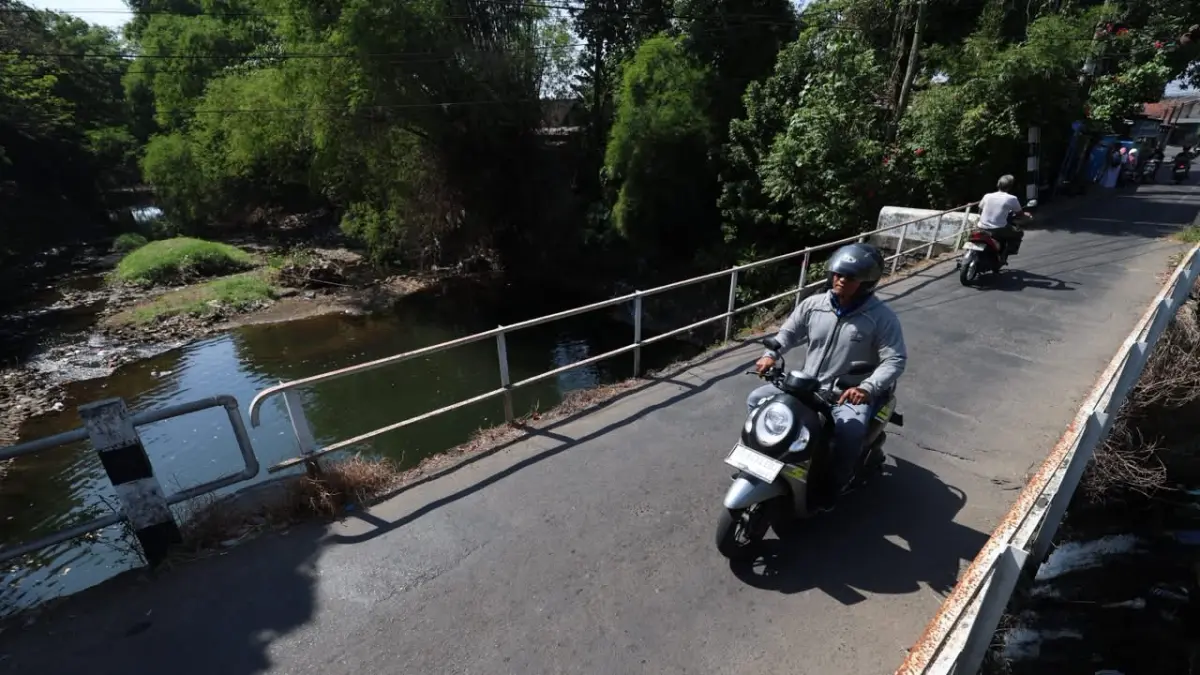 PENGHUBUNG: Pengendara motor melintas di Jembatan Gang 4 Kelurahan Bujel. Sungai Kedak di bawahnya punya peran penting dalam menghubungkan aliran sungai lereng Gunung Wilis menuju muaranya di Sungai Brantas. (Foto: Wahyu Adji)