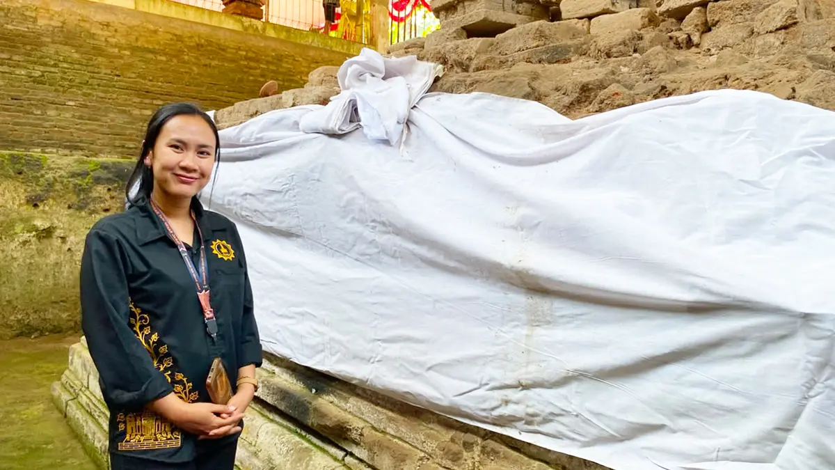 PENGABDIAN: Nila Yusia, jupel Candi Dorok berpose di latar salah sudut bangunan bersejarah di Desa Manggis, Kecamatan Puncu. (FOTO: Emilia Susanti/JPRK)