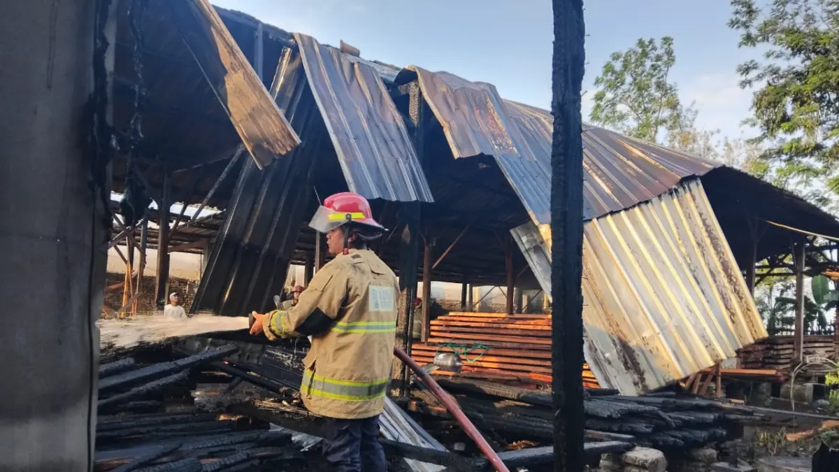 Petugas Pemadam Kebakaran Kabupaten Kediri menyemprotkan air ke puing-puing gudang kayu yang terbakar.