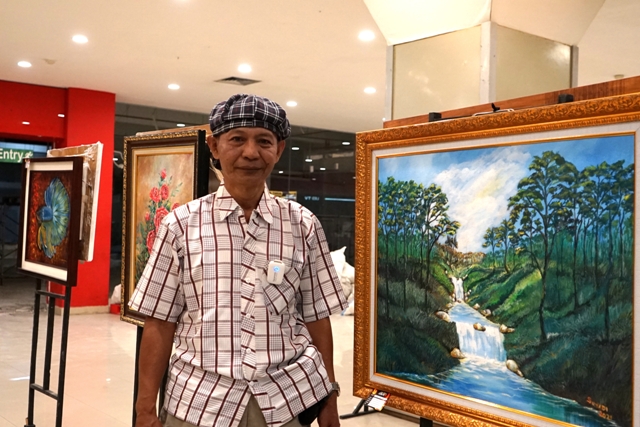 DEDIKASI: Suyadi berada di dekat karya lukisnya yang dipamerkan di salah satu pusat pertokoan di Kediri kemarin. (Foto: Ilmidza Amalia Nadzira)