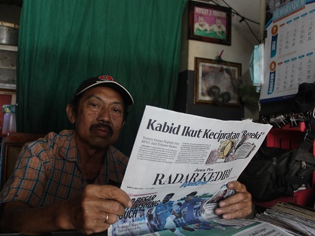 CATAT TAGIHAN: Suparman, pemilik agen koran Sakti, di Desa Tulungrejo, Kecamatan Pare saat sedang membaca Jawa Pos Radar Kediri. (Foto: Iqbal Syahroni)