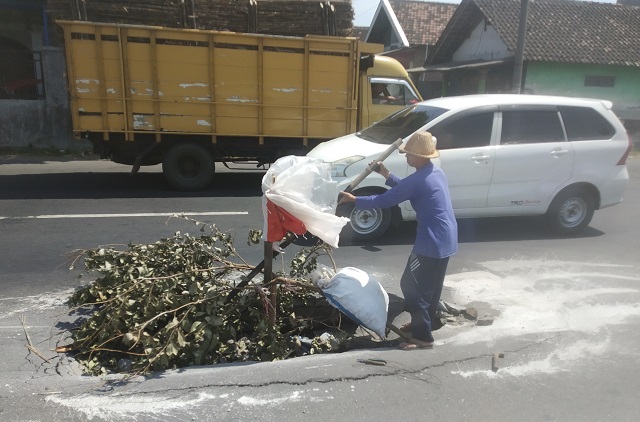 BUTUH PERHATIAN:  Supilan memberi tanda dengan dahan pohon, bamboo dan karung di jalan rusak berlubang, Jalan Pamenang, Desa Sumberejo, Kecamatan Ngasem (25/7). (Khalqinus Taaddin/JPRK)