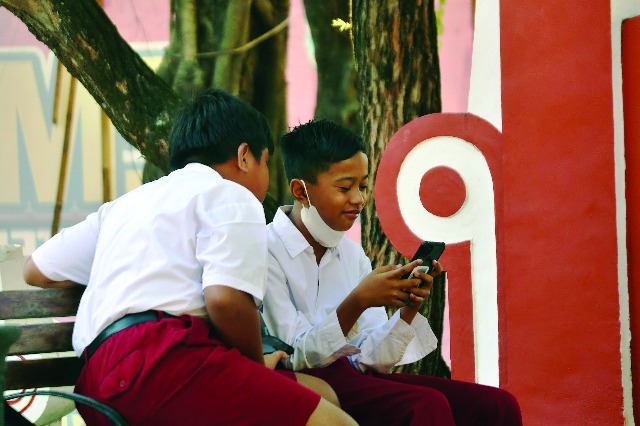 TAK BISA LEPAS HP: Siswa SD di Nganjuk bermain games di handphone saat pulang sekolah. Orang tua harus membatasi penggunaan handphone. (Foto: Karen Wibi)