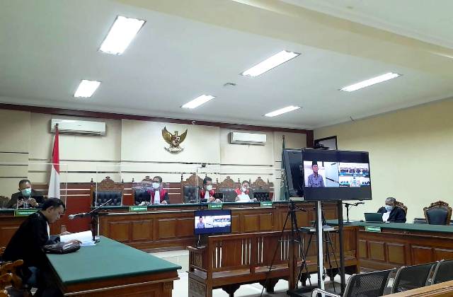 DI MONITOR: Terdakwa Bambang ditampilkan melalui layar televisi saat menjalani sidang online di PN Tipikor Surabaya kemarin. (Foto: Iqbal Syahroni)