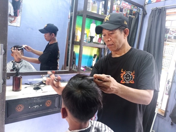 MURAH: Kinaryo Hadi memangkas rambut pelanggannya di Desa Pehkulon, Papar. Dia hanya mematok tarif Rp 5 ribu per orang. (Foto: Rekian)