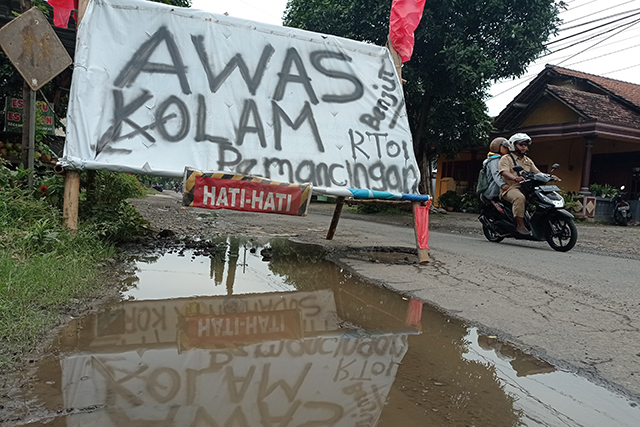 RAWAN CELAKA: Warga Desa Mondo, Kecamatan Mojo memasang banner di Jalan Utama Kediri-Tulungagung karena jalan yang berlubang itu jadi biang kecelakaan. (Foto: Wahyu Adji)