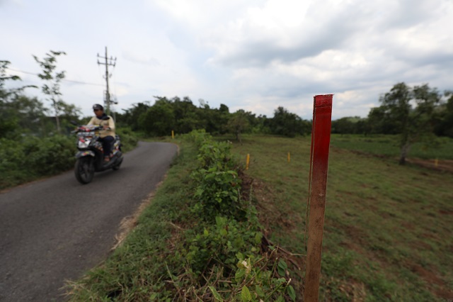 DARI BAMBU: Warga melintas di dekat patok bambu warna merah yang tertancap di jalur yang akan dilewati tol Kediri-Tulungagung, di Desa Manyaran, Kecamatan Banyakan. (Foto: Wahyu Adji)