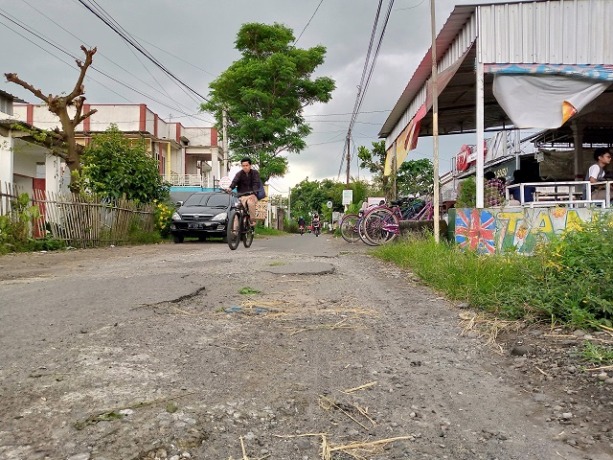 MENGELUPAS: Seorang pengendara melintasi jalanan di Kampung Inggris yang sudah rusak di sana-sini. (Foto: Rekian)