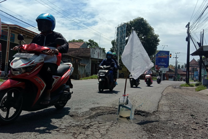 CEGAH KEJEGLONG: Pengendara melintasi jalas aspal berlubang yang ditancapi galon dengan bendera plastik putih di tikungan Sonorejo, Wonoasri di Kecamatan Grogol (4/3). (Foto: Asad)