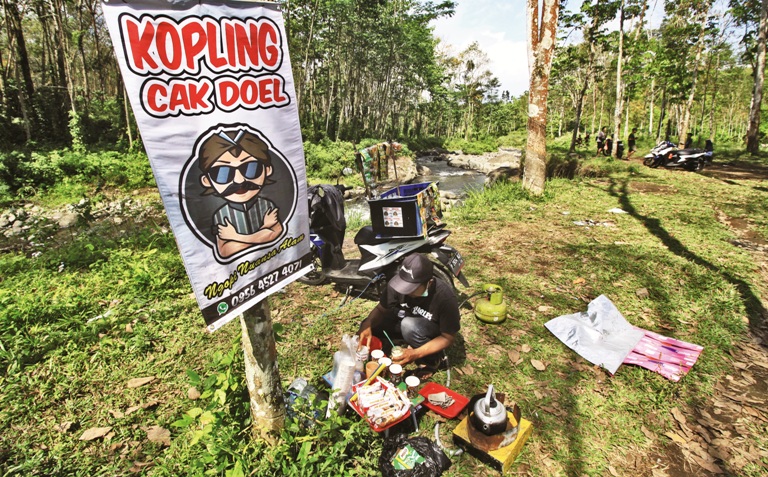 MERACIK: Cak Doel membuat kopi yang dijual di pinggir sungai dekat hutan karet di Desa Klungkung, Kecamatan Sukorambi, Jember, kemarin (6/7).