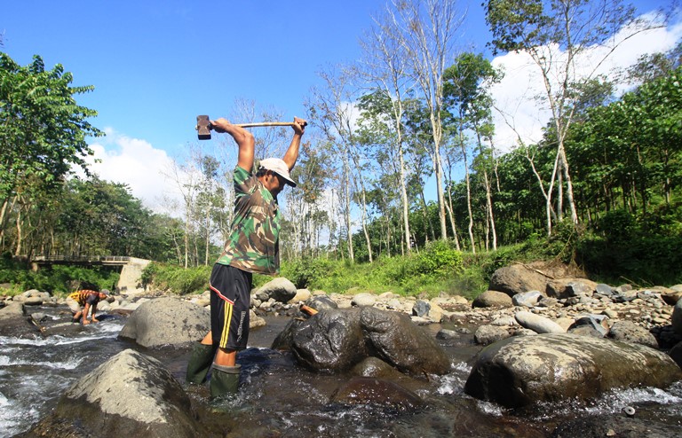 KERJA KERAS: Solihin, buruh pemecah batu, menggunakan palu untuk memecah batu di Sungai Jompo, Desa Klungkung, Kecamatan Sukorambi.