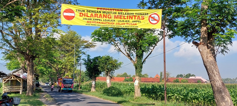 DEMI JALAN ASPAL: Pemerintah Desa Ampel dan Desa Lojejer, Kecamatan Wuluhan, kompak memasang spanduk larangan kendaraan muatan berat melebihi tonase melintas di jalan desa setempat.