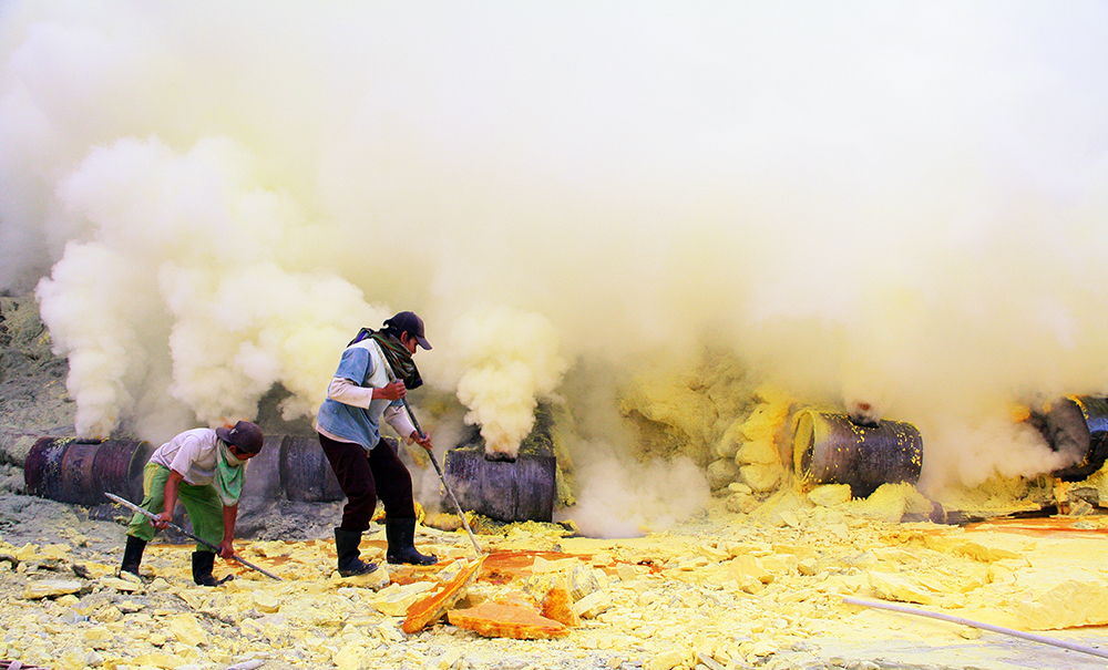DISELIMUTI BELERANG: Penambang mengambil belerang yang telah mengeras di dasar Kawah Ijen.