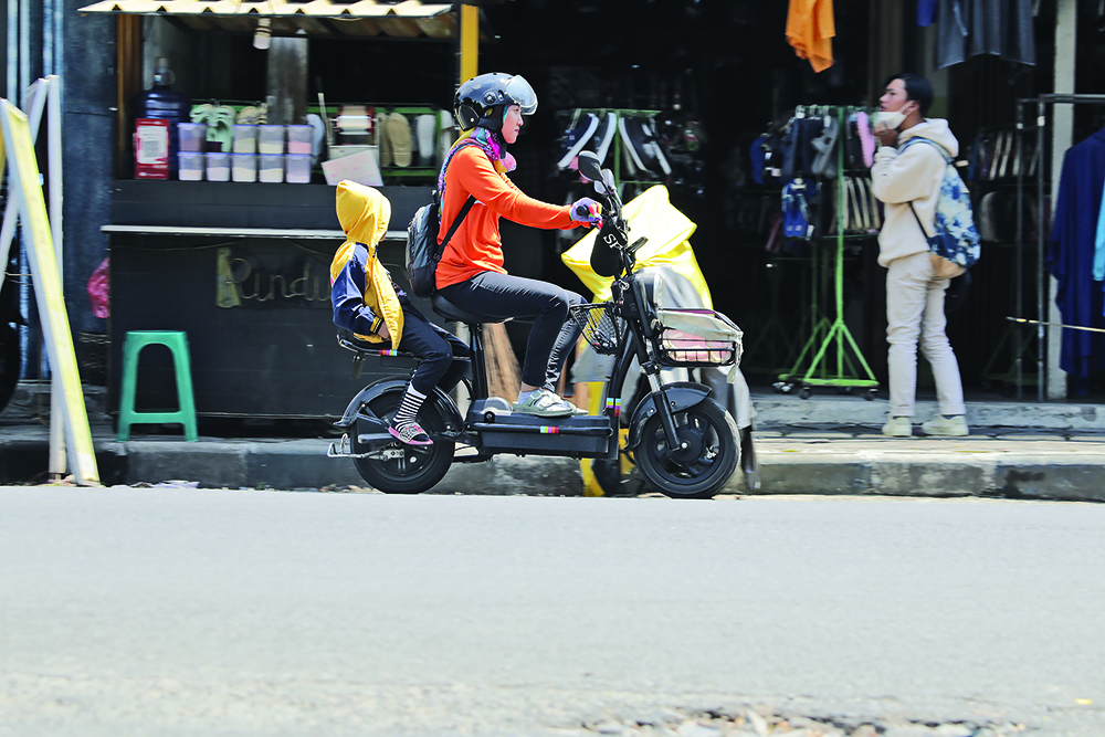 HARUS HATI-HATI: Warga membonceng putranya menggunakan sepeda listrik di Jalan Kalimantan, Jember, kemarin.