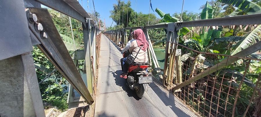 HATI-HATI: &nbsp;Pengendara motor yang melintas di jembatan gantung Desa Sabrang, Kecamatan Ambulu. Kini jembatan tersebut mulai terdapat pagar, sementara kawat bajanya tidak ada.