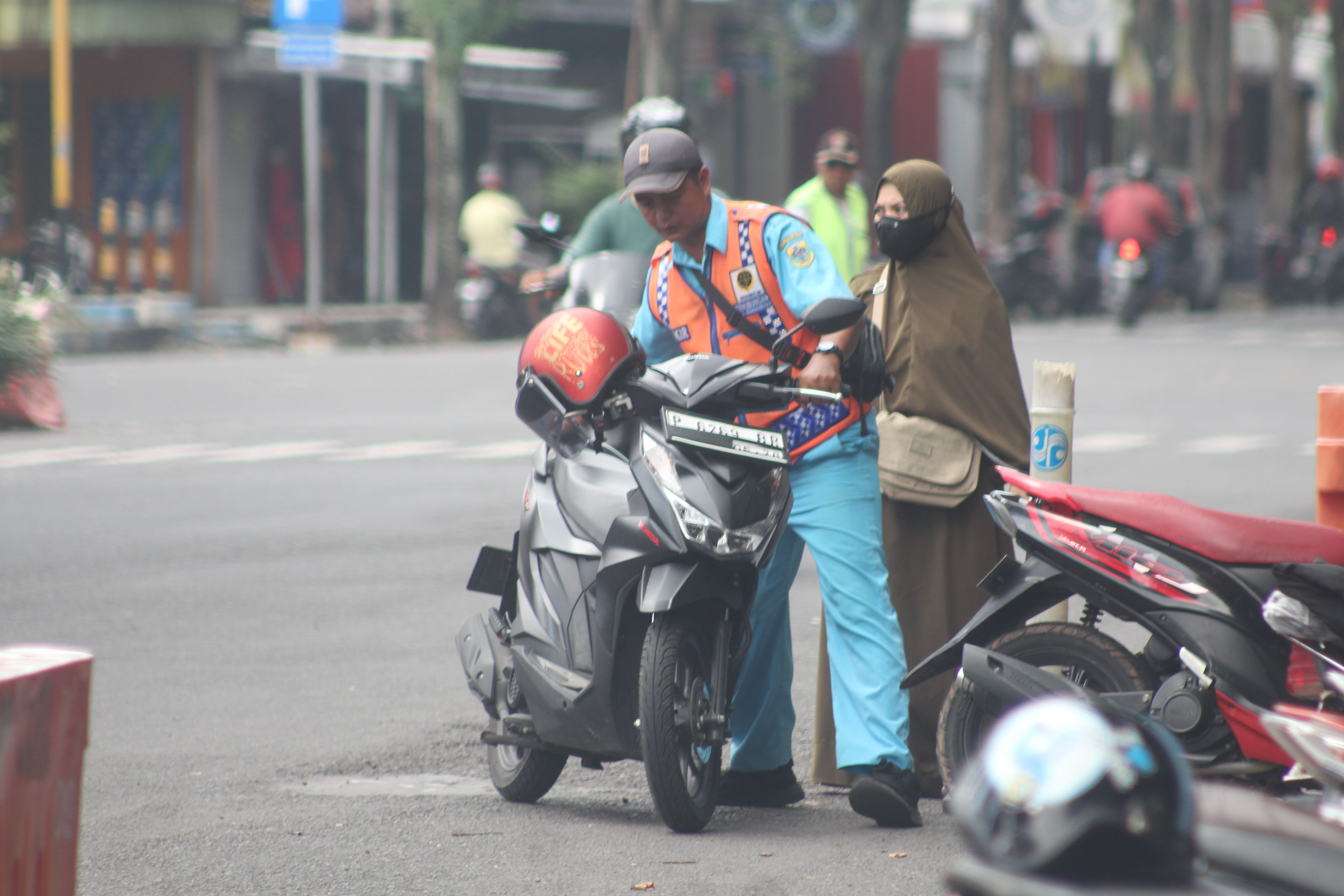 PARKIR: Seorang jukir tengah membantu pengendara yang hendak meninggalkan Alun-Alun Bondowoso.