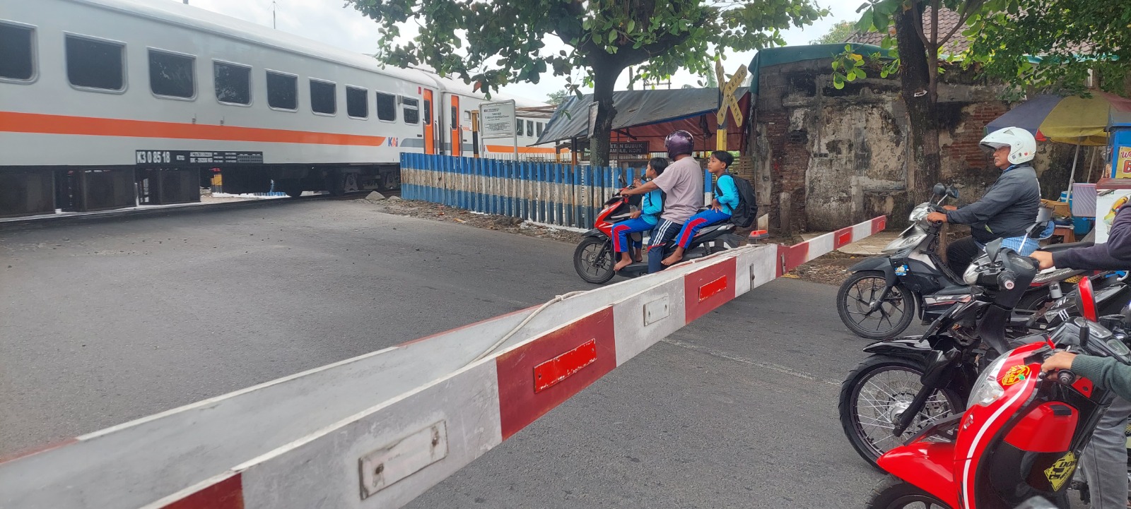 BAGAIMANA INI: Seorang bapak membonceng dua putranya yang baru pulang sekolah, menerobos palang pintu lintasan kereta api di Mangli, kemarin. (JUMAI/RADAR JEMBER)