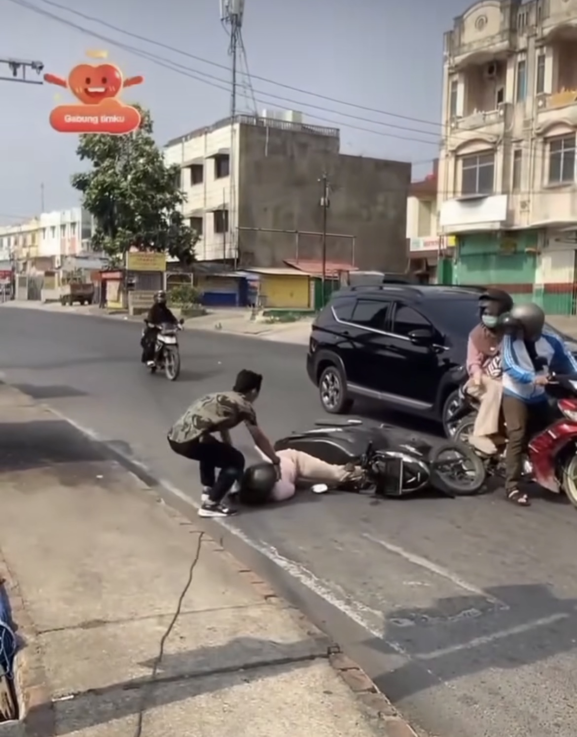 Seorang pengamen membantu pemotor yang terjatuh.