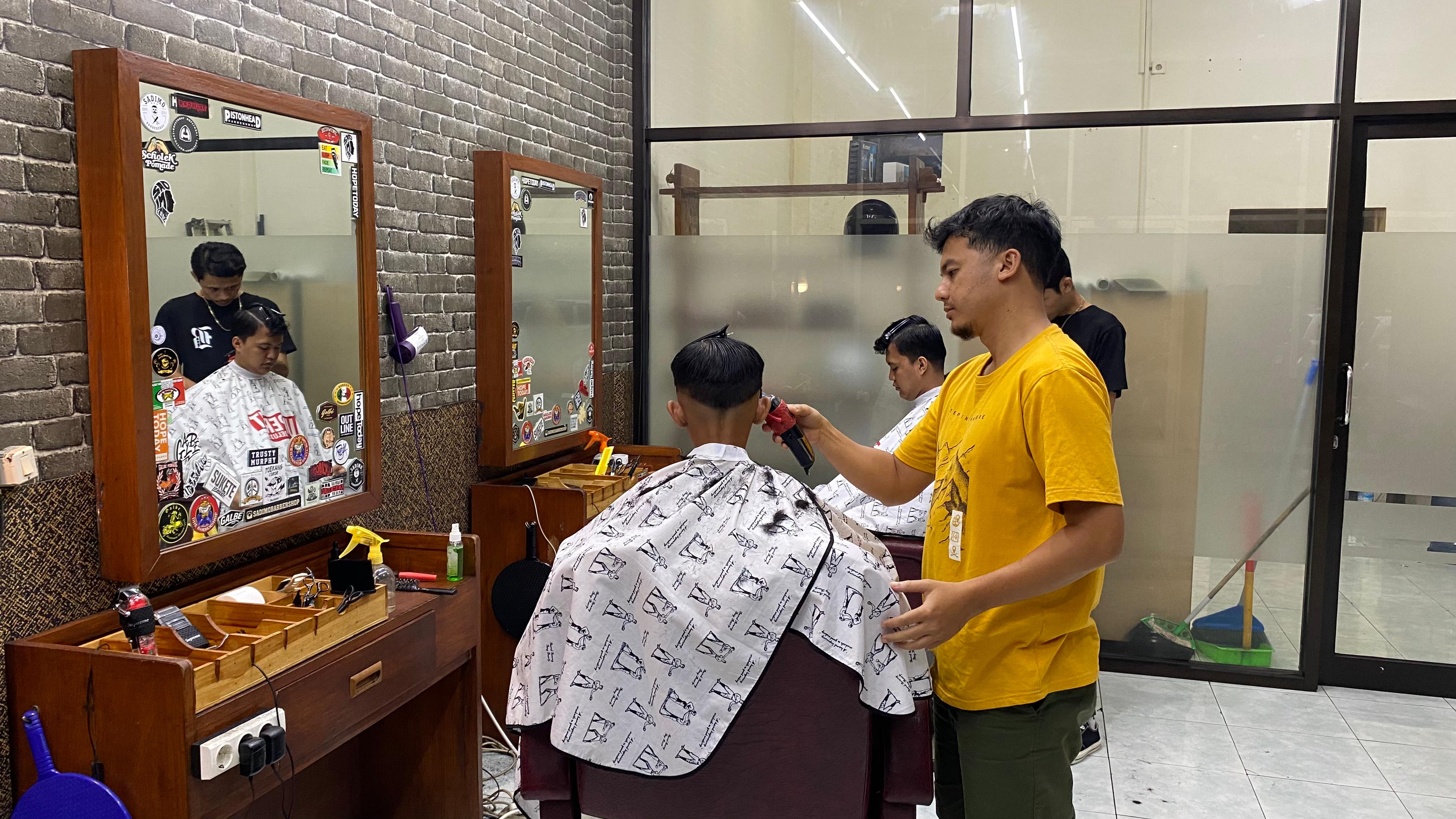 PUNYA SKILL: Mahfud Fendi saat memangkas rambut pelanggannya. Berawal dari belajar di salon. Sekarang sudah miliki tiga cabang Barbershop di Jember.(VINGKY SETIAWAN/ RADAR JEMBER)