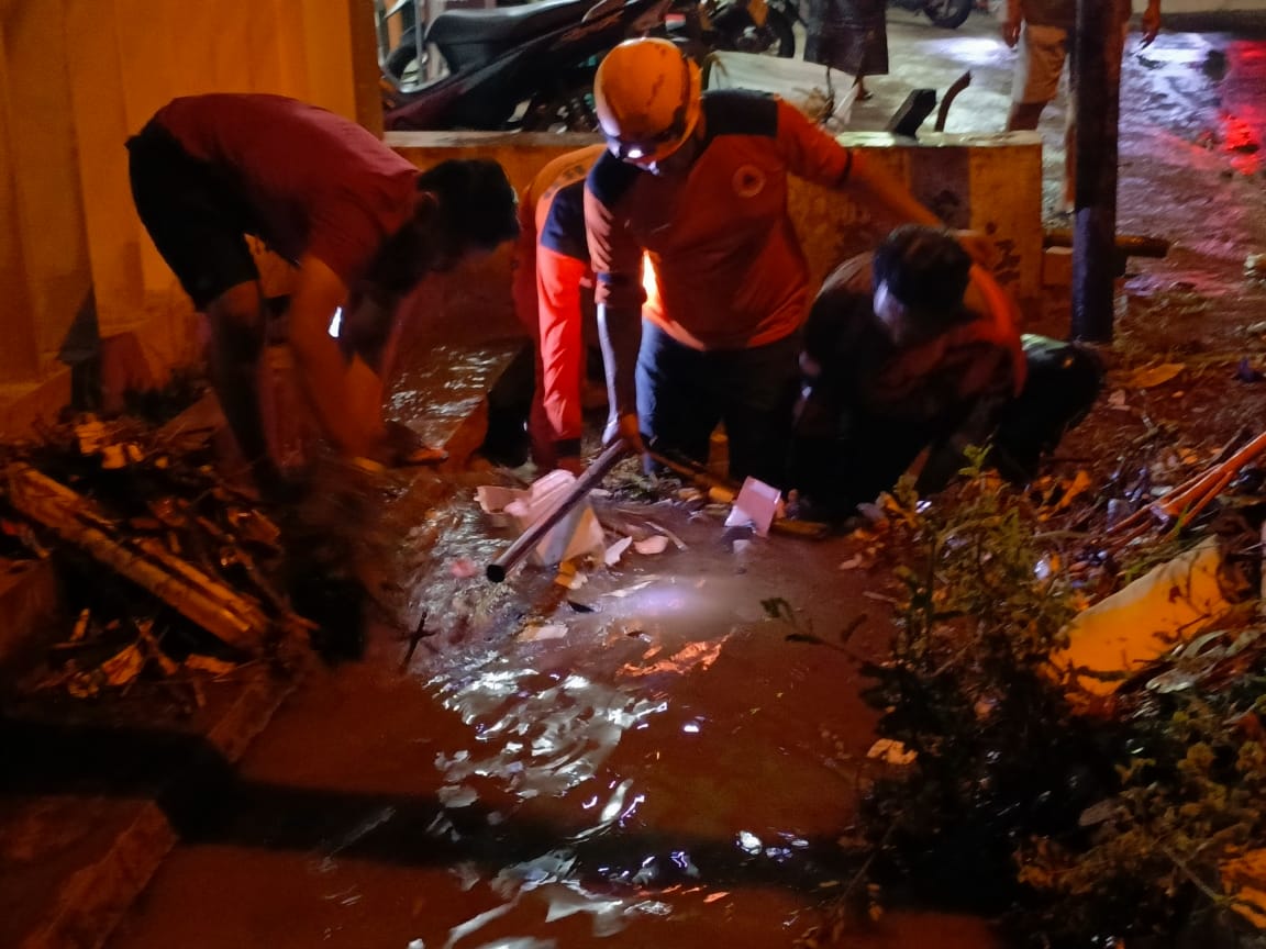 TERSUMBAT: Petugas saat membersihkan saluran drainase yang tersumbat akibat banjir, di Kelurahan Badean.