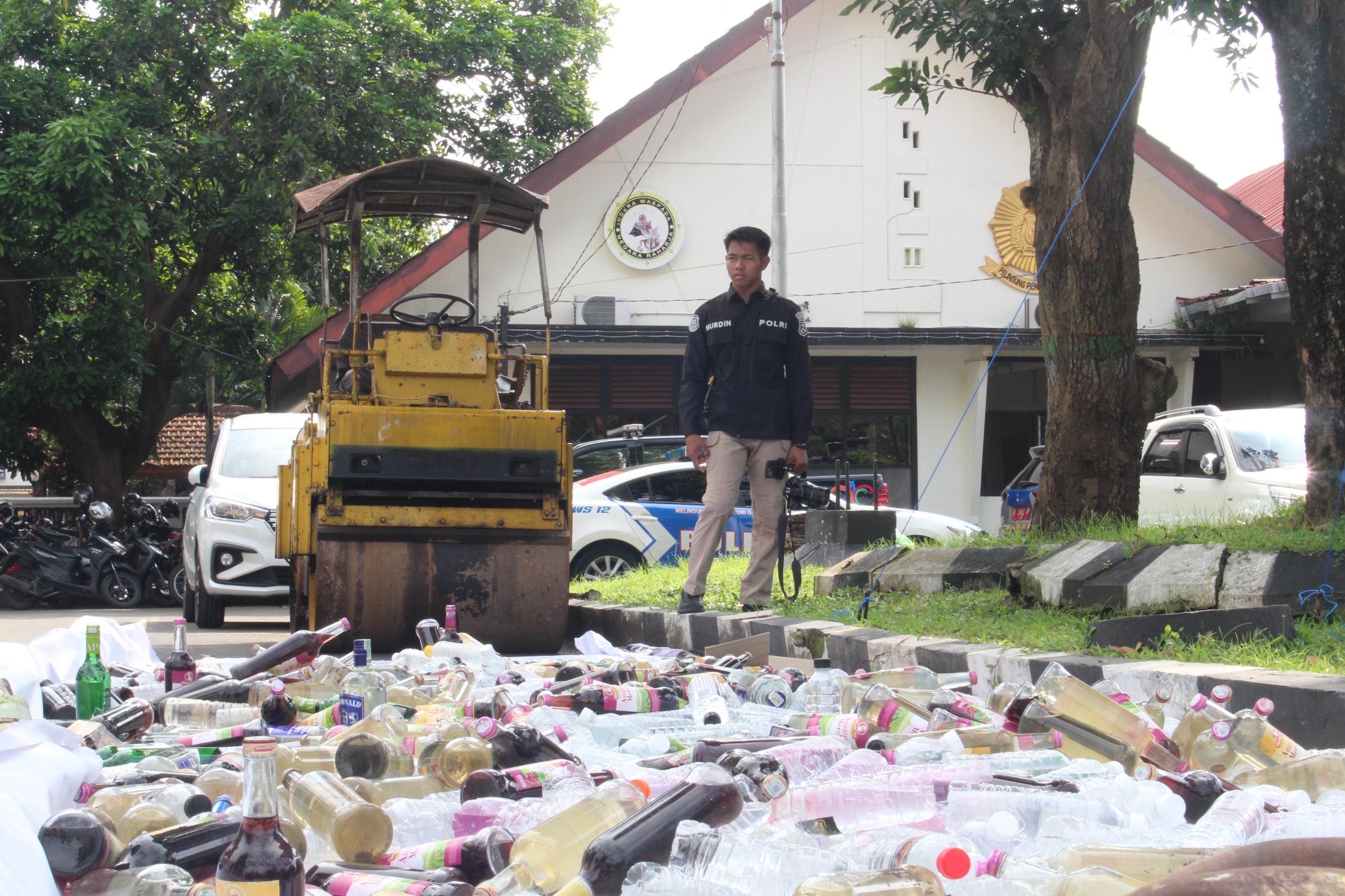 DIMUSNAHKAN: Petugas bersiap menghancurkan ratusan botol miras menggunakan alat berat.