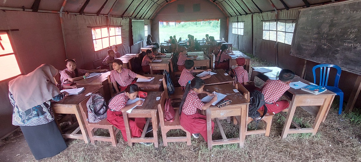 KBM DI TENDA: Siswa SDN Plalangan 03, Kecamatan Kalisat, Jember, mengikuti KBM di bawah tenda milik BPBD Jember sejak ruang kelas ambruk, Sabtu (23/11/2024), hingga saat ini. (JUMAI/RADAR JEMBER)