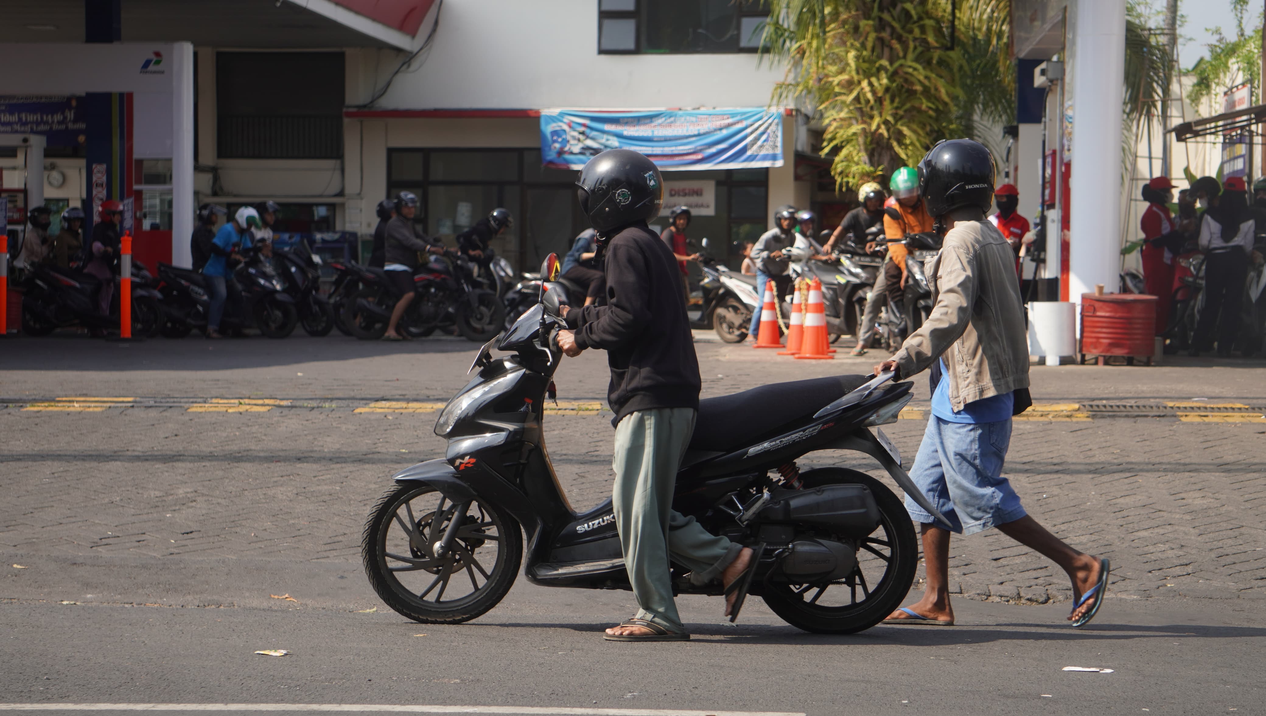 KEHABISAN BENSIN: Pengendara motor di jalan gajah mada mendorong motonya yang tengah kehabisan bensin, Sabtu 27/7 (Foto Yulio FA/Radar Jember)