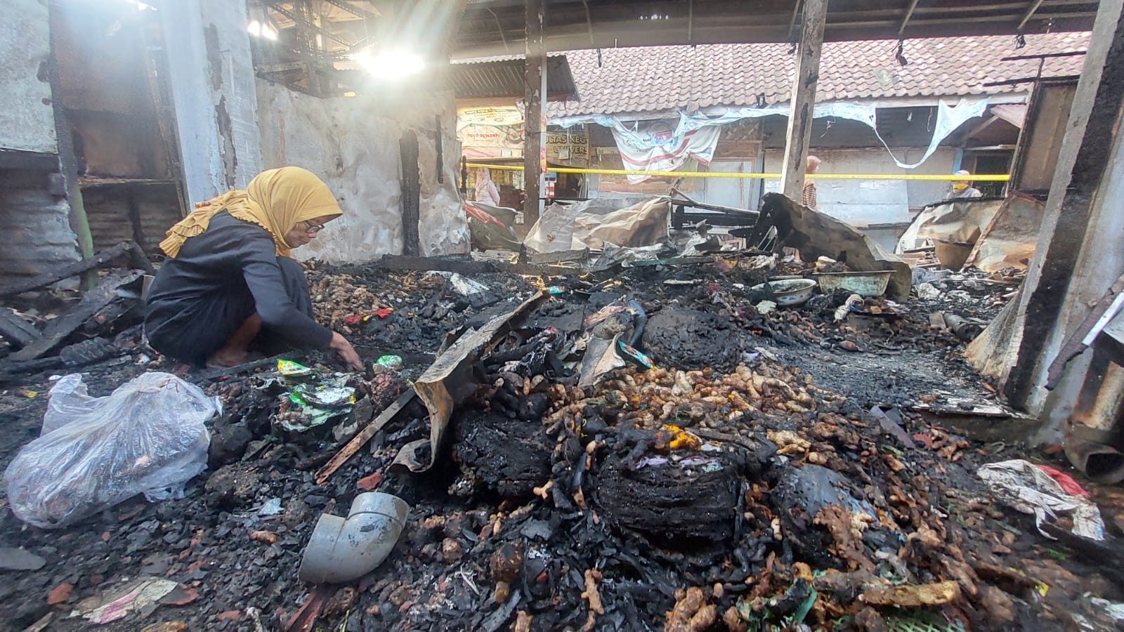CARI SISA KEBAKARAN: Jumaiya, 65, pemilik lapak saat pasar Tradisional rambipuji terbakar pada Senin (11/8/2025) mencari sisa barang-barang yang terbakar.(JUMAI/RADARJEMBER).
