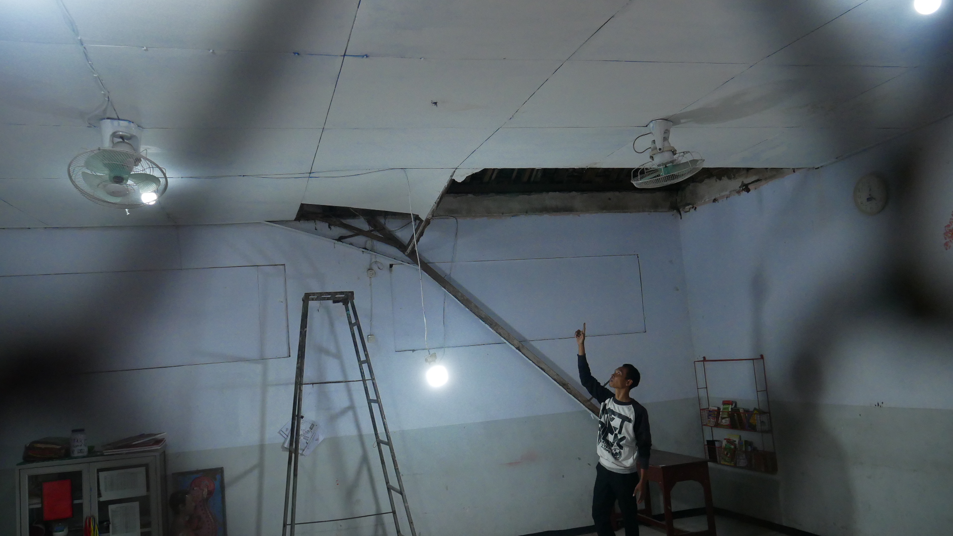 RUSAK: Imam, satpam sekolah menunjukkan kondisi plafon yang ambrol di ruang kelas 6 SDN Gebang 01 Jember, kemarin (26/8).