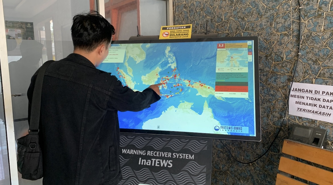 DIPANTAU: Salah seorang warga bersama petugas BPBD Bondowoso melihat monitor yang memperlihat kejadian gempa di seluruh Indonesia.(ILHAM WAHYUDI/RADAR IJEN)
