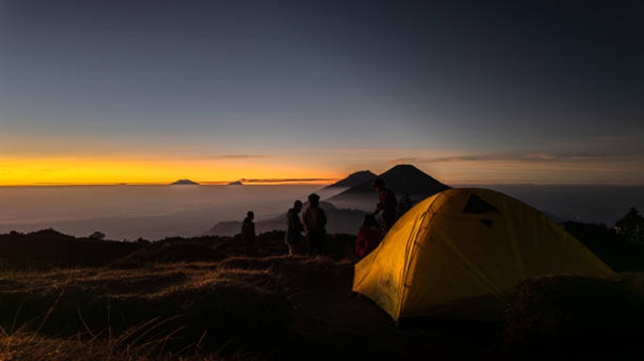 Wonosobo, Indonesia - August 30, 2024: Hikers are waiting for sunrise moment at Mount Prau peak in Dieng, Wonosobo, Indonesia with clear red sky background.