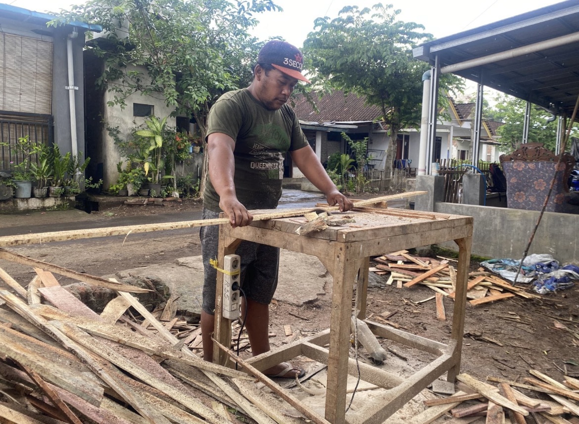 TELATEN: Fathor Herman memotong kayu untuk dijadikan kotak sayur dan cabai di rumahnya, dia memiliki banyak pekerja lansia.(ILHAM WAHYUDI/RADAR IJEN)