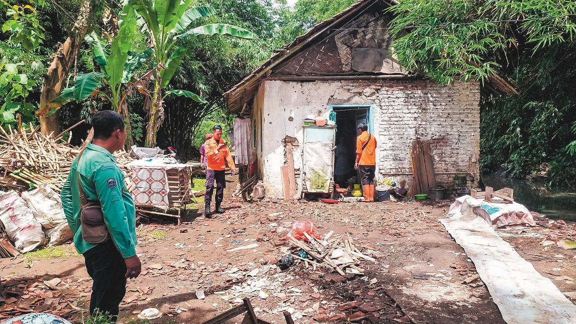 TURUN LANGSUNG: Personel BPBD Jember meninjau rumah yang ambruk dan menyerahkan bantuan kepada warga terdampak.