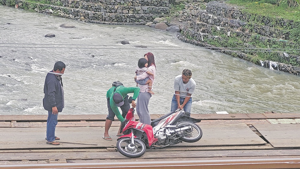 DITOLONG PEKERJA: Seorang ibu bersama anaknya ditolong pekerja proyek jembatan kereta api di Dusun Krajan Selatan, Desa Patemon, Kecamatan Pakusari karena terjatuh, di jembatan darurat, Minggu (18/1).