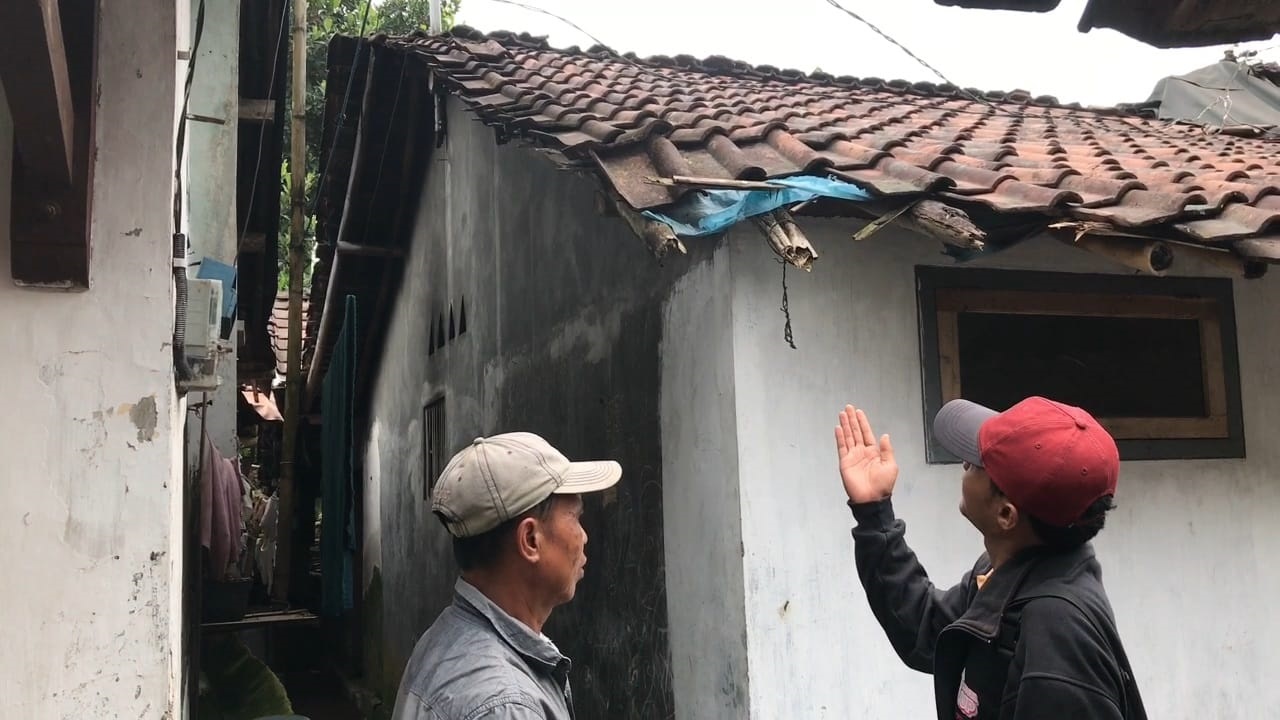 TRAGIS: Ketua RW setempat, Suharjo, menunjukkan genting rumah korban yang sempat terkena kayu milik pelaku.