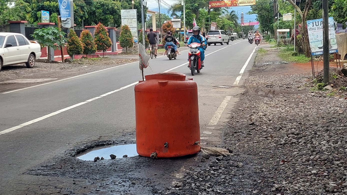 BIAR LEBIH AMAN: Warga di pinggir Jalan Raya Desa Pancakarya, Kecamatan Ajung, memasang tandon air bekas sebagai penanda jalan berlubang agar pengendara lebih waspada.&nbsp;