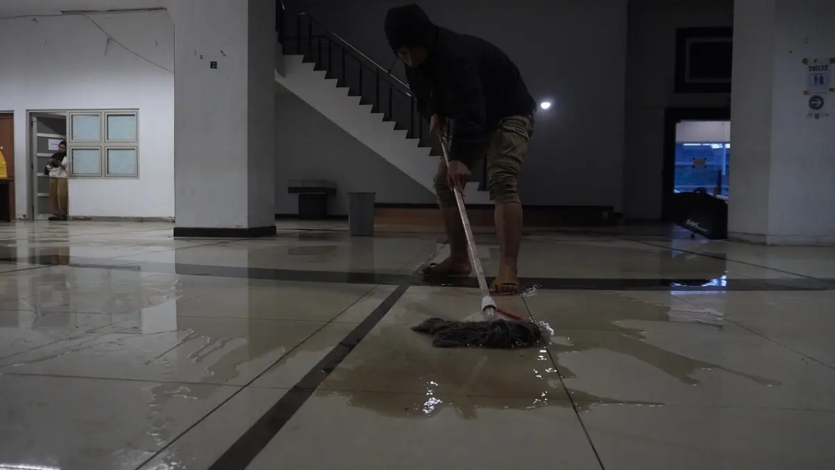 PEL SENDIRI: Salah satu warga mengepel lantai Lobi Stadion JSG yang bocor saat hujan deras beberapa waktu lalu. (SIDKIN ALI/RADAR JEMBER)