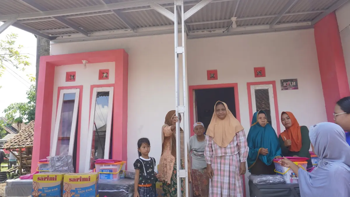 HARAPAN BARU: Keluarga Sumiati, warga di Dusun Karang Sirih, Desa Suco, Kecamatan Mumbulsari, yang tak kuasa menahan haru bahagia saat rumahnya telah bersolek dengan sisi depannya kombinasi antara warna penuh cinta atau pink dengan putih. (MAULANA/RADAR JEMBER)