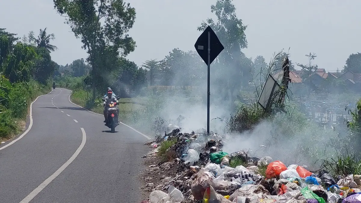 GANGGU PENGGUNA JALAN: Pengendara sepeda motor yang hendak ke Pantai Puger terganggu dengan asap sampah yang dibakar. (JUMAI)