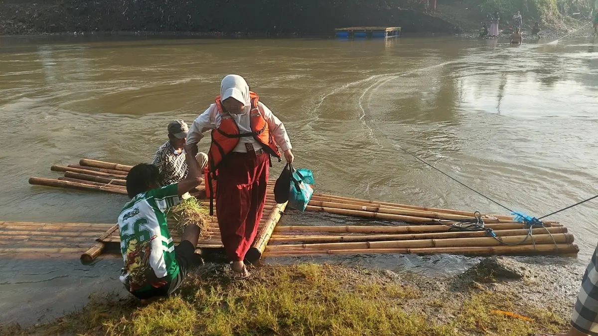 KEMBALI NAIK GETEK: Siswa SDN Jubung 02 berangkat dan pulang sekolah menggunakan getek bambu yang ditarik warga untuk menyeberangi sungai. (JUMAI/RADAR JEMBER)