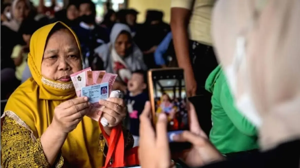 Petugas memotret warga memperlihatkan uang tunai saat penyaluran bantuan sosial di Kota Tangerang, Banten, Selasa. (12/8/2025).(Putra M. Akbar/ANTARA)