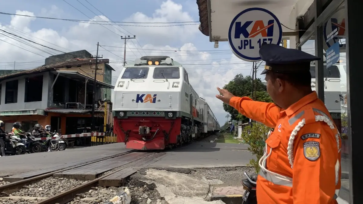 SIAGA: Salah satu penjaga palang pintu perlintasan kereta api, ketika melambaikan tangan kepada masinis. (DOKUMENTASI RADAR JEMBER)