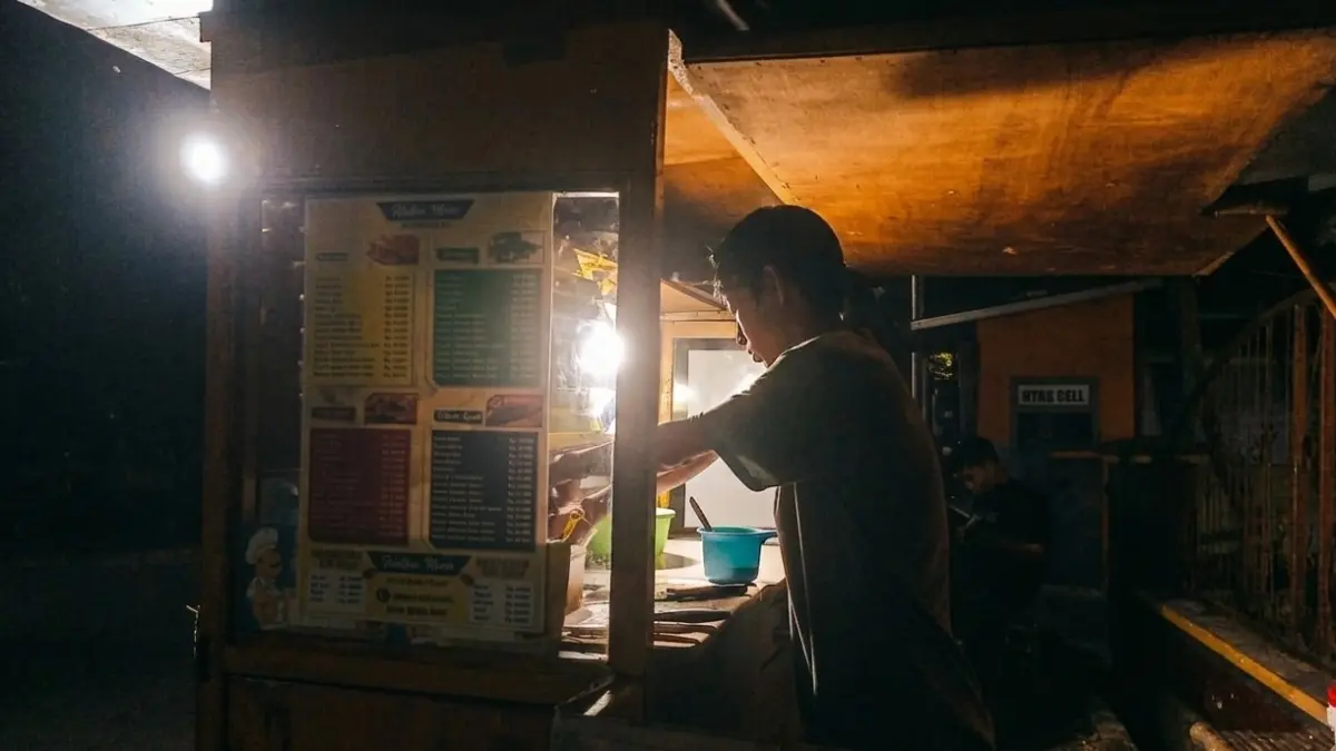 KEMBALI BERJUALAN: Arifin, warga Kelurahan Kranjingan, Sumbersari, melayani pelanggan yang membeli martabak, Rabu (10/6). Akibat pemadaman listrik, ia mengaku penjualannya terganggu. (SIDKIN ALI/RADAR JEMBER)

