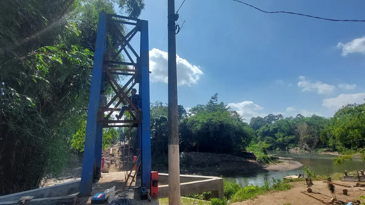 INFRASTRUKTUR: Dua pekerja menyelesaikan konstruksi jembatan gantung di Desa Jubung, Kecamatan Sukorambi. Jembatan tersebut sebelumnya putus karena banjir pada Januari 2026 lalu. (JUMAI/RADAR JEMBER)