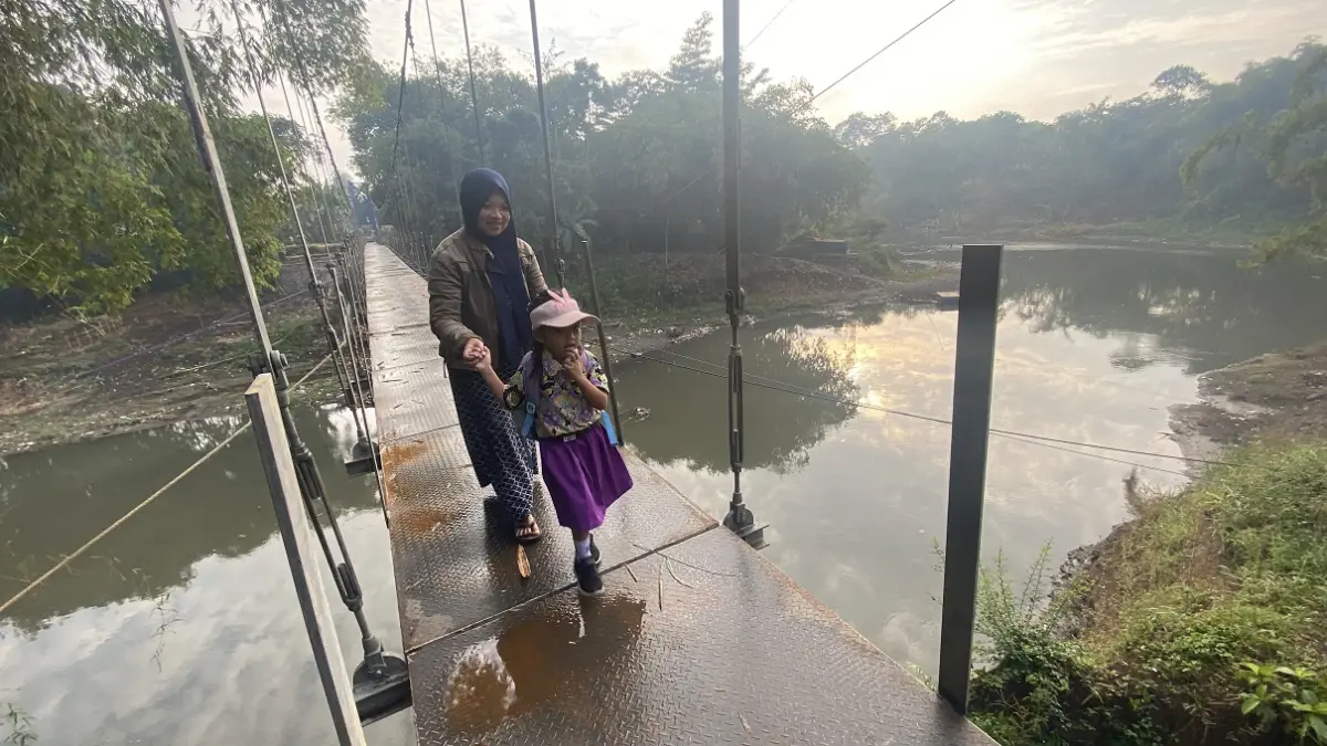 LICIN: Orang tua mengantarkan anaknya sekolah dengan melewati Jembatan Jubung yang belum selesai seluruhnya. (JUMAI/RADAR JEMBER)