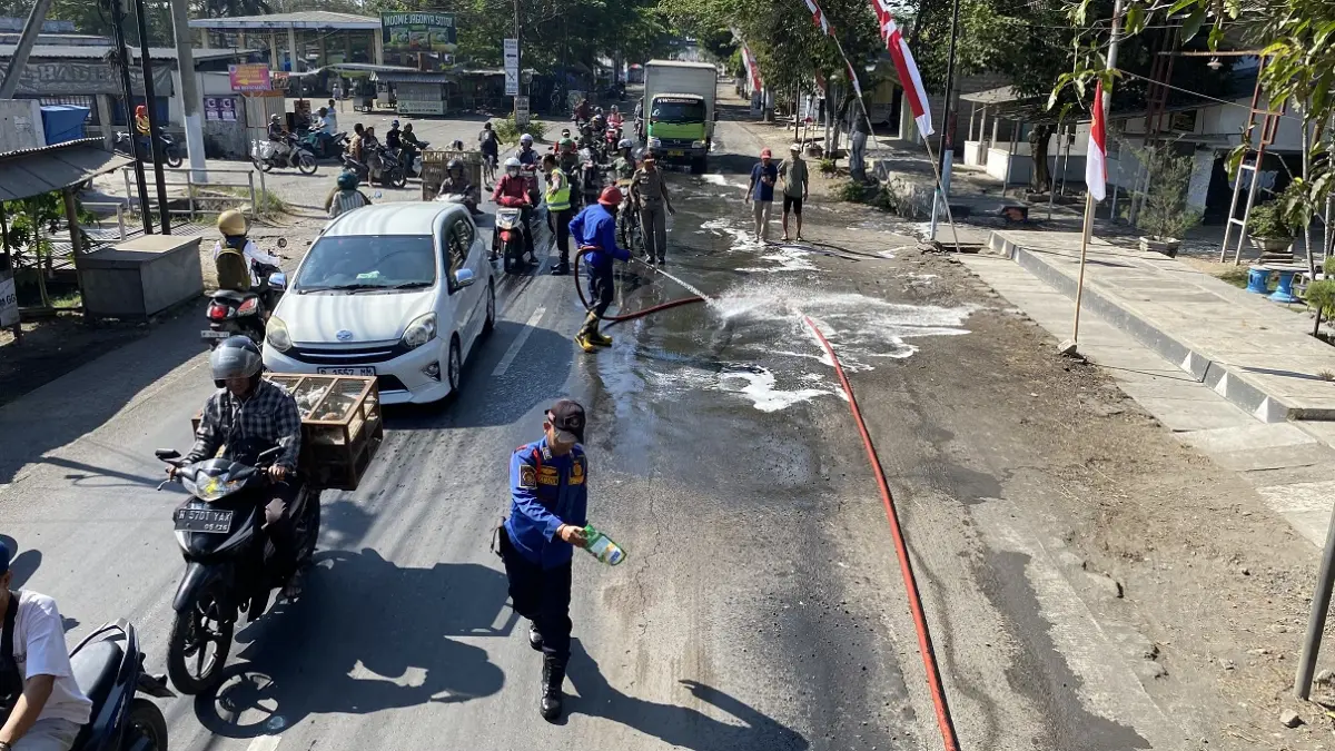 PEMBERSIHAN: Petugas Damkar Posko Jember melakukan penyemprotan ceceran solar di Jalan Diponegoro, Kecamatan Kencong, kemarin (26/8) pagi. (JUMAI/RADR JEMBER)

